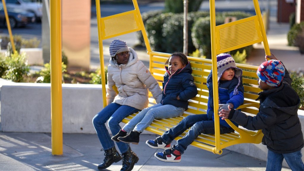 Four children sit on a yellow bench swing at Five Points Plaza