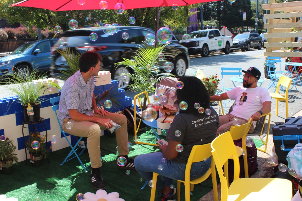 People sit in the UDC's parklet with bubbles and fun seating on Parking Day 2025