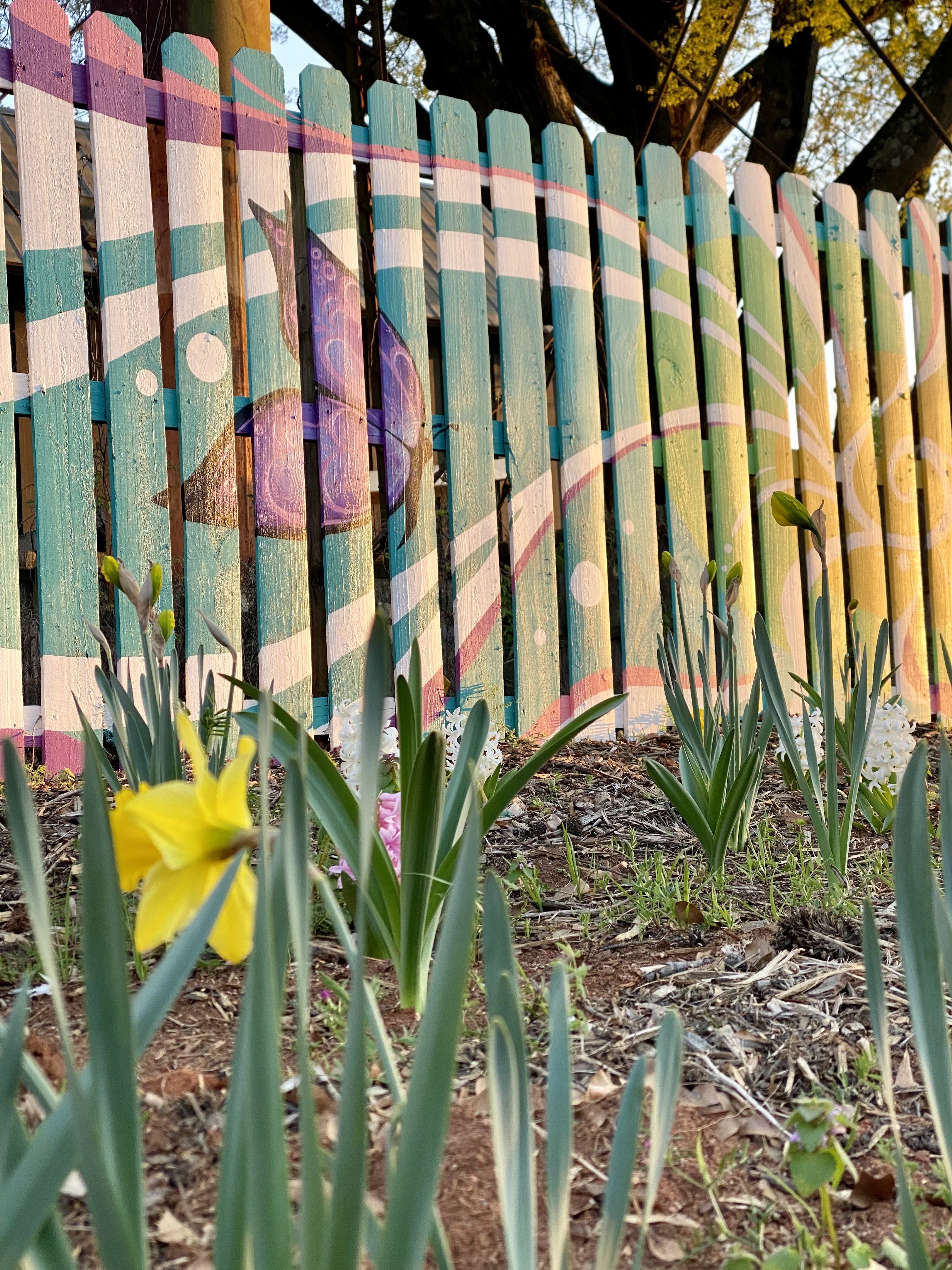 flowers bloom in front of a butterfly mural on a fence