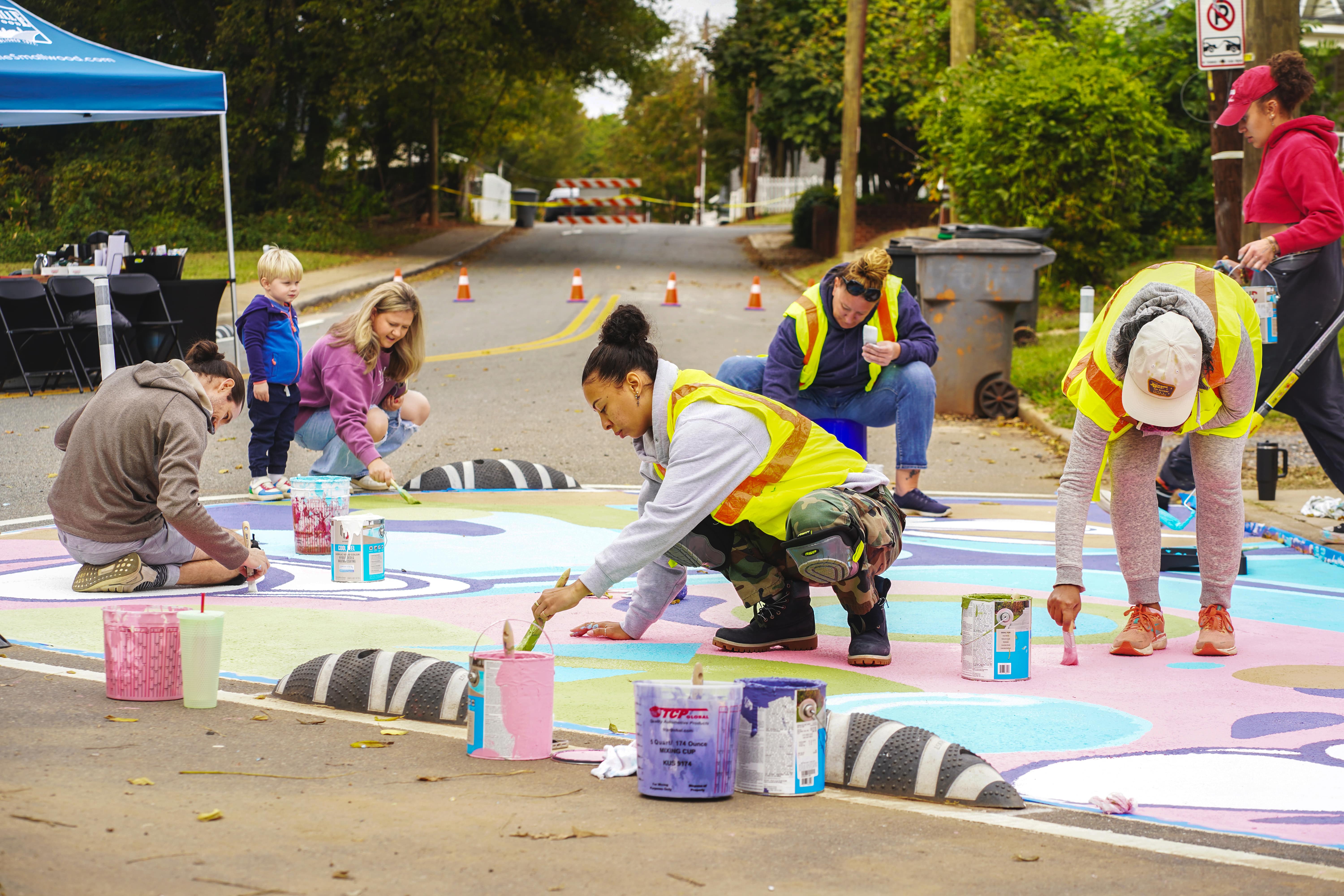 Volunteers paint a street mural at Trade and Solomon intersection to improve pedestrian visibility